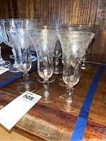 Nine vintage cordial glasses with etched Morning Glory floral design on stems, displayed on a wooden surface.