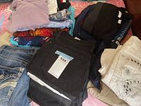 Folded men's clothing including denim jeans, black jeans, and various shirts on bed