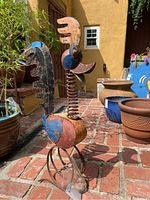 Photo of metal roadrunner garden sculpture on brick patio, showing front-side view with colorful painted metal and spring neck detail.