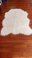 Full view of white shag rug on wooden floor, showing pelt style with organic edges and fluffy texture.
