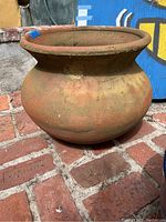 Photo showing side view of the large rounded terracotta pot sitting on brick floor with visible weathering