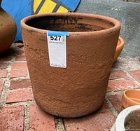 Front view of a large terracotta planter on brick surface showing textured surface and sticker label