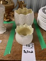 Two Belleek porcelain bowls with fluted and scalloped edges on a wooden surface with other items in the background