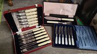 Birks and Unett fork and knife sets shown in open red and black cases with cream-colored handles and silver blades.