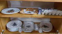 Overall view on two wooden shelves showing various Christmas-themed dinnerware, platters, shakers, napkin rings