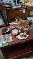 Photo showing Beswick ceramic horse, Limoges Pastaud creamer, Goebel Friar Tuck creamers on tray, glass ashtray, serving spears, Pelin Thorley creamer and sugar cup, wood table surface