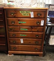 Front view of a medium brown Pepplers wooden dresser with six drawers, metal handles, some staining, and green tape on some handles.