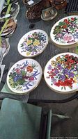 Photo showing several plates with detailed floral patterns placed on a table, showcasing gold rims and vibrant multi-colored flower illustrations.
