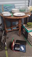 Front and top view of wooden gateleg table with dishes and various small items on top (not included in lot). Table has turned legs and medium wood finish.