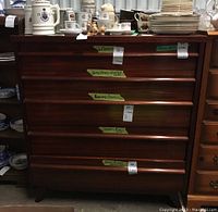 Front view of five-drawer wood dresser with various ceramic items on top, seller tags on drawers