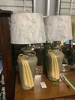 Pair of earthenware table lamps with mottled gray base and yellow sash stripe decorations, with white marbled lampshades, placed side by side on wooden surface in front of mirror.