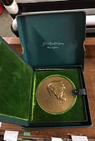 Open presentation case showing bronze medal seated in green velveteen interior with lid open.