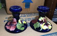 Pair of Moorcroft candle holders with various colors of hibiscus flowers and dark blue background