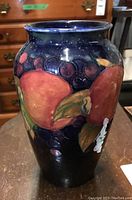 Front side view of Moorcroft vase showing pomegranate and grape cluster design with glossy finish.