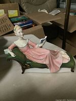 Clear image showing the figurine reclining on a green chaise lounge, emphasizing the detail in the pink dress and facial features.