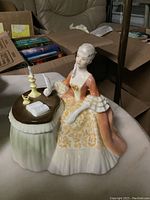 Angle showing front and side of Royal Doulton figurine with woman seated at table holding quill pen.