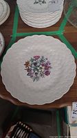Top-down view of white ceramic platter with multicolored flower bouquet in center and embossed floral edge pattern.