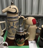 Photo of three ceramic beer steins including two tall bird-shaped lid steins and one smaller blue relief design stein.