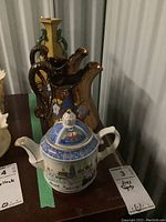 Photo shows blue and white teapot in front with two gold-toned floral-print jugs and a gold handled vase behind.