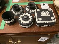 Top view of seven Wedgwood jasperware china pieces on wooden surface, showing detailed white relief classical designs on matte black bodies.