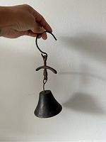 Front view of the antique cast iron bell showing the full length from the curved hook to the bell base.