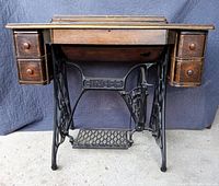 Front view of antique Singer sewing machine cabinet with treadle base, showing wood drawers and pedal.