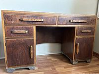 Front view of burlwood desk showing two large top drawers and lower drawers and cabinets with brass handles.