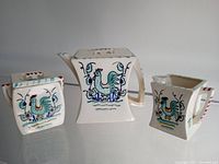 Photo showing front and side views of teapot, creamer, and sugar bowl with colorful rooster designs and pastel accents.