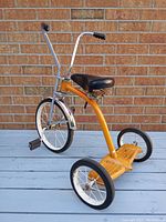 Front and side view of the orange vintage muscle trike showing chrome ape hanger handlebars and padded black seat.