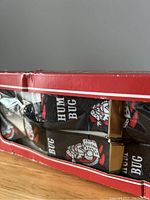 Close-up photo showing the elastic suspenders with a black background and 'HUM BUG' lettering and Santa Claus design, partially visible inside the box.