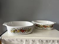 Photo showing side view of two Corningware casserole dishes with Spice of Life decoration, side handles visible