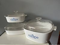 Three Corningware ovenware dishes with Blue Cornflower pattern, each with glass lids.