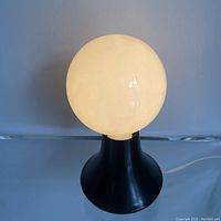 Front view of lamp showing white frosted glass globe bulb and flared black base on flat surface.