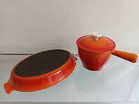 Levcoware pot with lid and Descoware baking dish side by side showing orange enamel finish and shape.