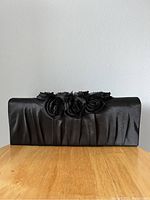 Front view of black satin clutch purse showing floral rosette embellishments