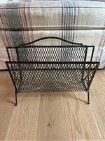 Front view of black iron metal magazine rack showing mesh diamond pattern and curved handle