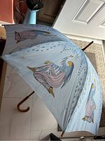 Light blue umbrella opened showing art print of woman sitting, raindrop detail, wooden handle visible.