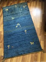 Full view of the handmade Persian Gabbeh wool rug laid out on wooden flooring showing its full rectangular shape, thick blue pile, and scattered colorful embroidered motifs.