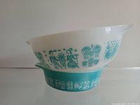 Side view showing larger white Pyrex mixing bowl with turquoise Butterprint pattern stacked on smaller turquoise casserole dish with white Butterprint design.