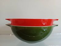 Side view of stacked red and green Pyrex Cinderella mixing bowls showing shape and size.