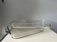 Two stacked clear rectangular glass baking dishes, one with handles, one without, showing the profile and transparency of ovenware.