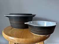 Two Pyrex Terra casserole dishes on wooden stool, one larger with lid, one smaller without lid