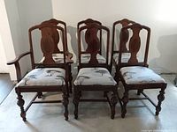Front view of all six solid walnut dining chairs showing detailed carved backs and upholstery