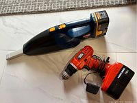 Ryobi hand vacuum and Black & Decker cordless drill placed on floor for item overview photo.