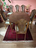 Photo of oval vintage wooden dining table with six chairs around it, table has a leaf in place. Chairs show carved wood details and light sage upholstery.