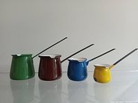 Photo showing the four graduated enamelware syrup or sauce warmers in green, dark red, blue, and yellow from left to right.