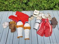 Full view of all 1960s vintage hockey gear displayed outside on a deck including gloves, pants, shin guards, helmet, elbow and wrist protective gear.