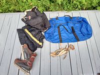 Photo showing full set of hockey pants, skates, suspenders, and blue equipment bag on a wooden deck outdoors