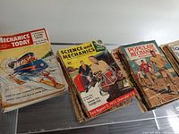Magazines spread showing Popular Mechanics Today, Science and Mechanics, Popular Mechanics with vintage illustrated covers featuring aircraft, motorcycles, and people.