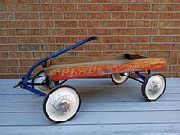 Side view of vintage Leader Meteor wagon showing wooden body with branding, blue metal frame, and white wheels with metal hubcaps.
